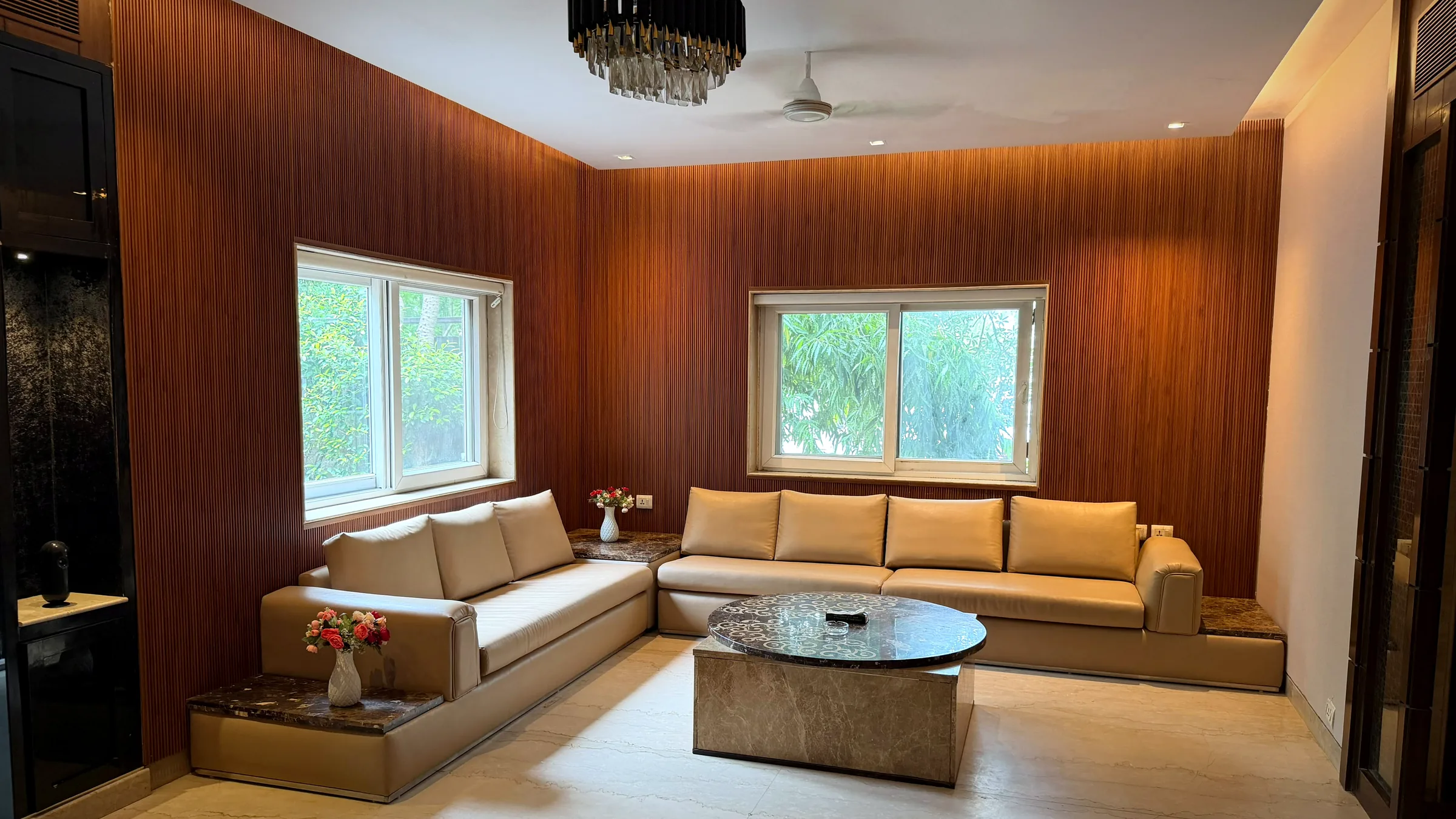Wood-panelled lounge with L-shaped sofa and garden-facing windows at Nivasa Villas, a 5 BHK luxury villa near CyberHub, Gurugram